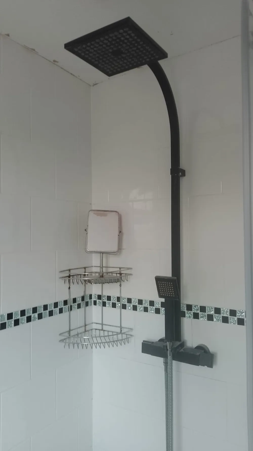 Matte black square shower head on a tall riser fitted in a corner shower