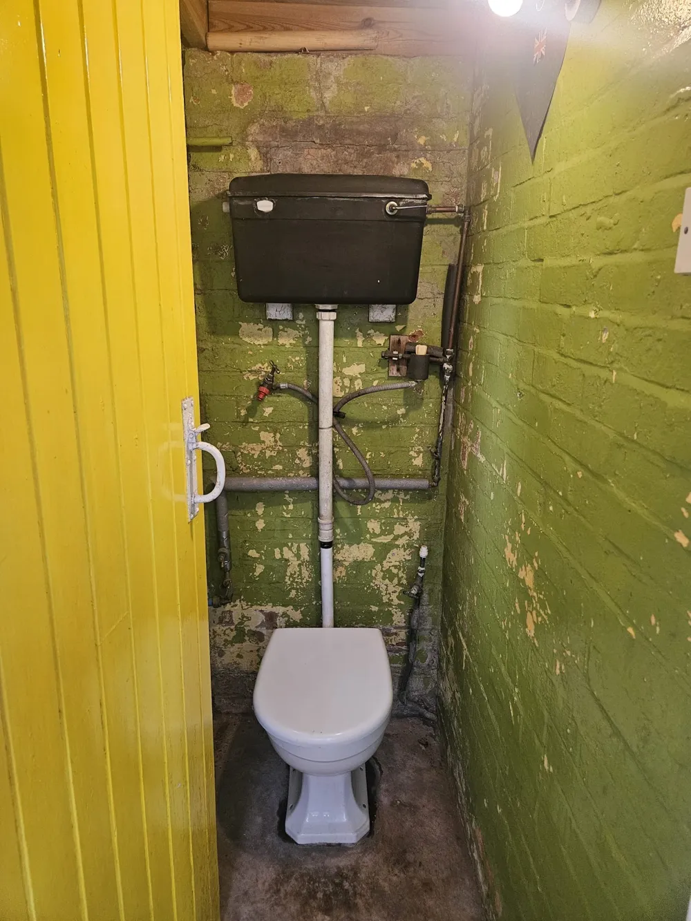 Old dated black cistern toilet with corroded pipework and flexi hoses before replacement in a Coventry outdoor WC